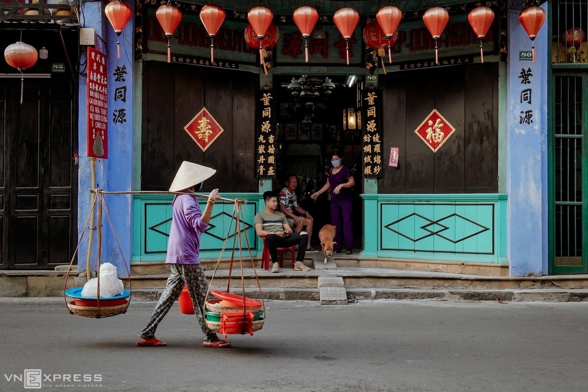 A woman carries a basket of rice cracker, a combination of baked coated cake, wet coated cake and some other materials, on her shoulder past a Chinese-style house on Nguyen Thai Hoc Street.